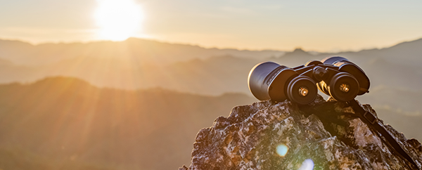 Pair of binoculars on a rock pointed toward a sunrise.